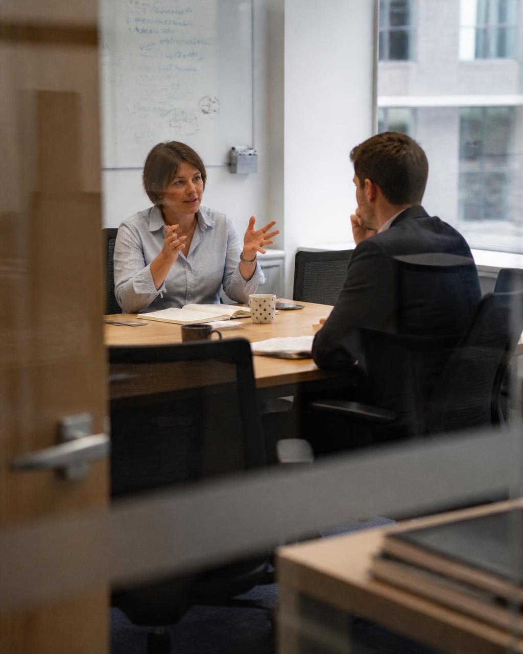 Two colleagues in conversation seen through a glazed doorway in flat daylight